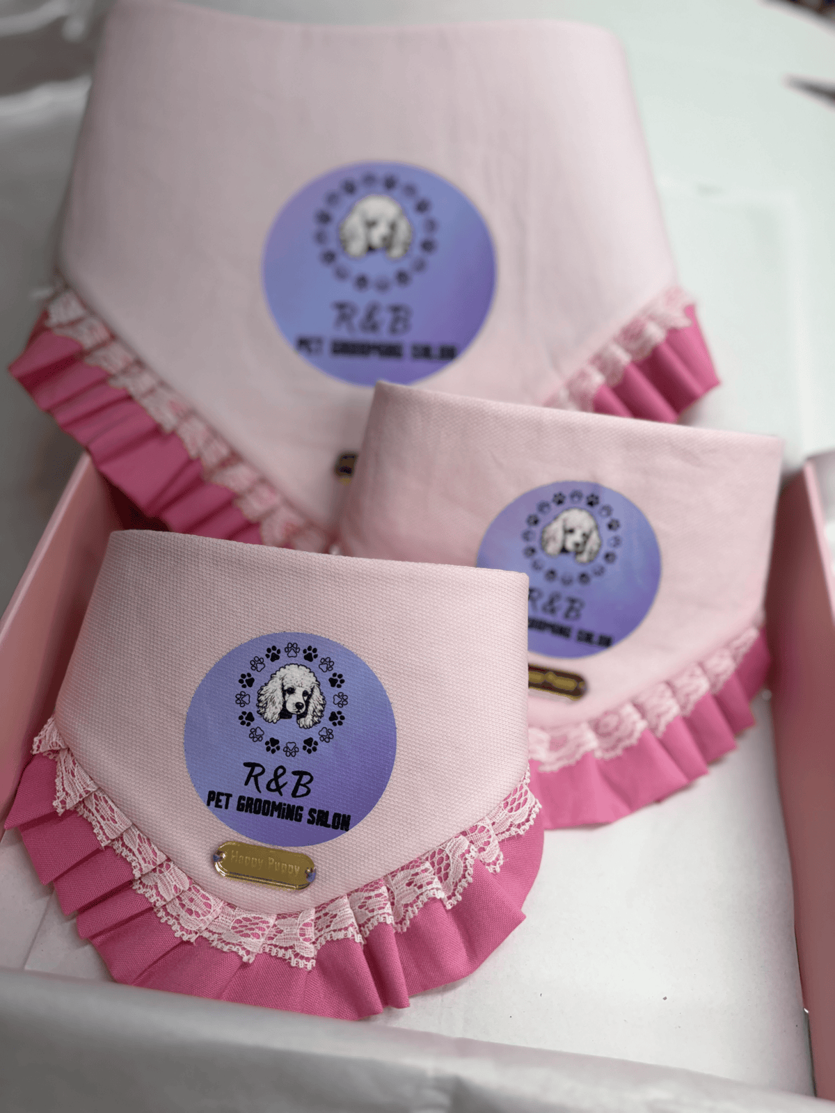 Bandanas para perro en rosa claro personalizadas con el logo circular de un salon de grooming, volante rosa con encaje, de Happy Puppy Bandanas