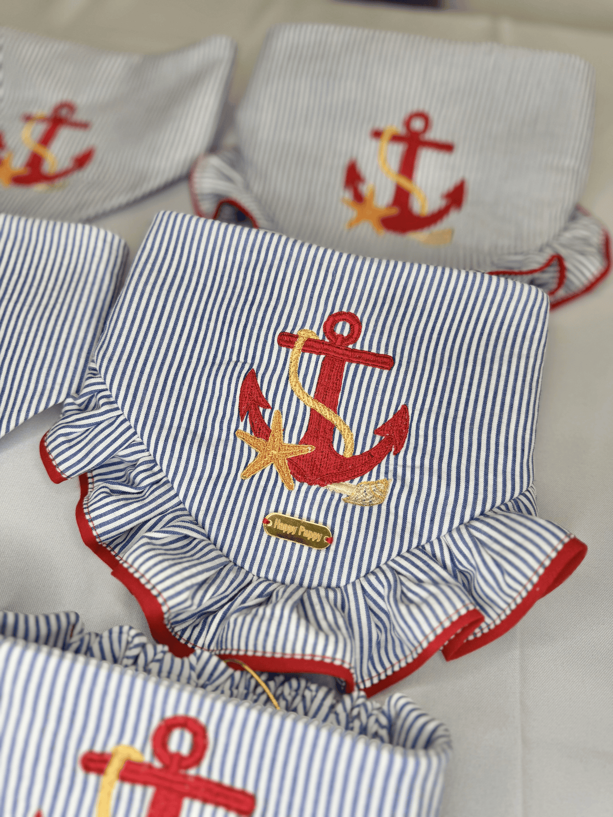 Detalle de la bandana para perro Beach Anchor de Happy Puppy Bandanas, rayas azul marino y blanco con ancla bordada en rojo y dorado y volante rojo
