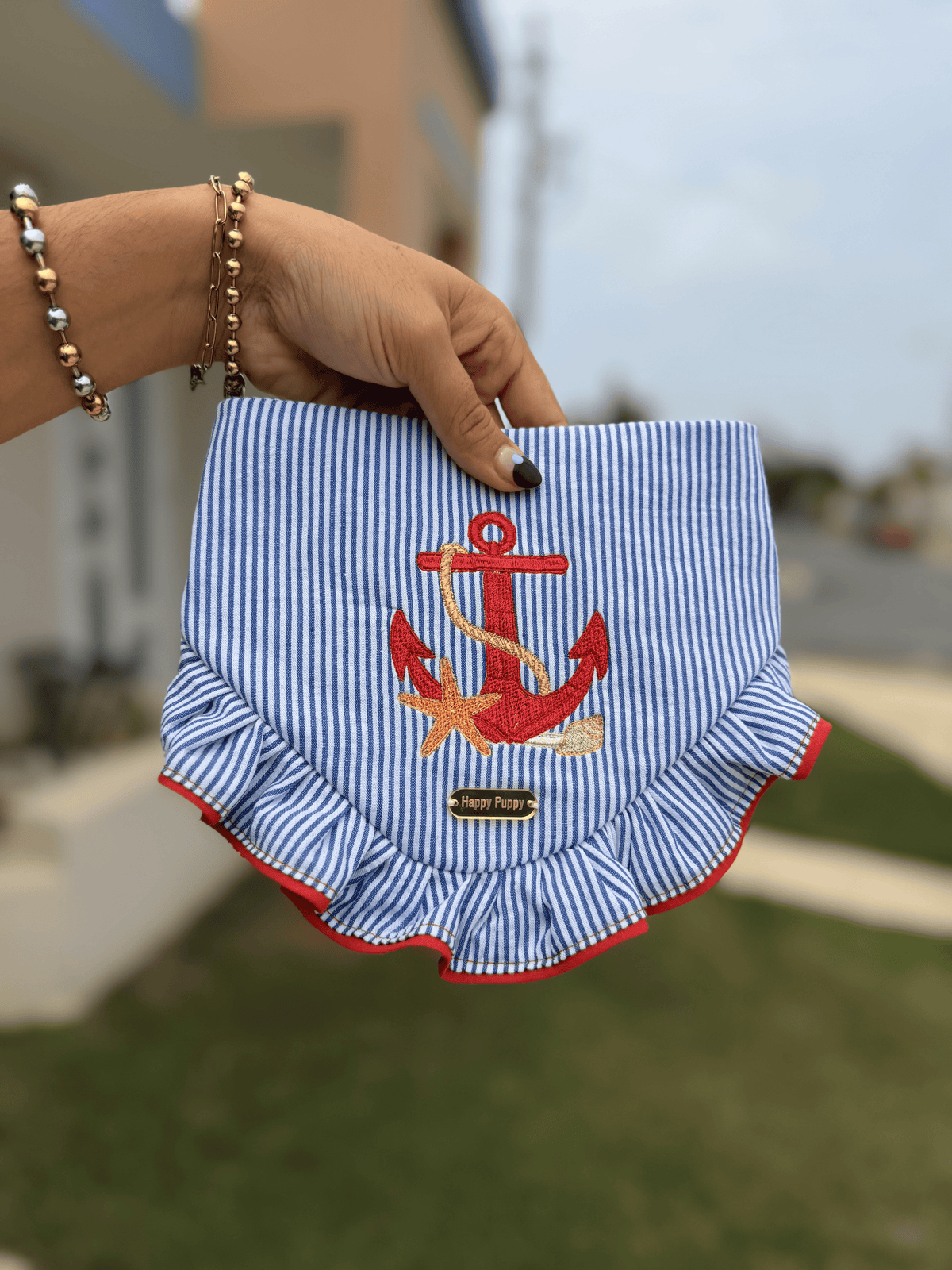 Bandana para perro Beach Anchor de Happy Puppy Bandanas en rayas azul marino con ancla bordada en rojo y volante, sostenida en la mano al aire libre