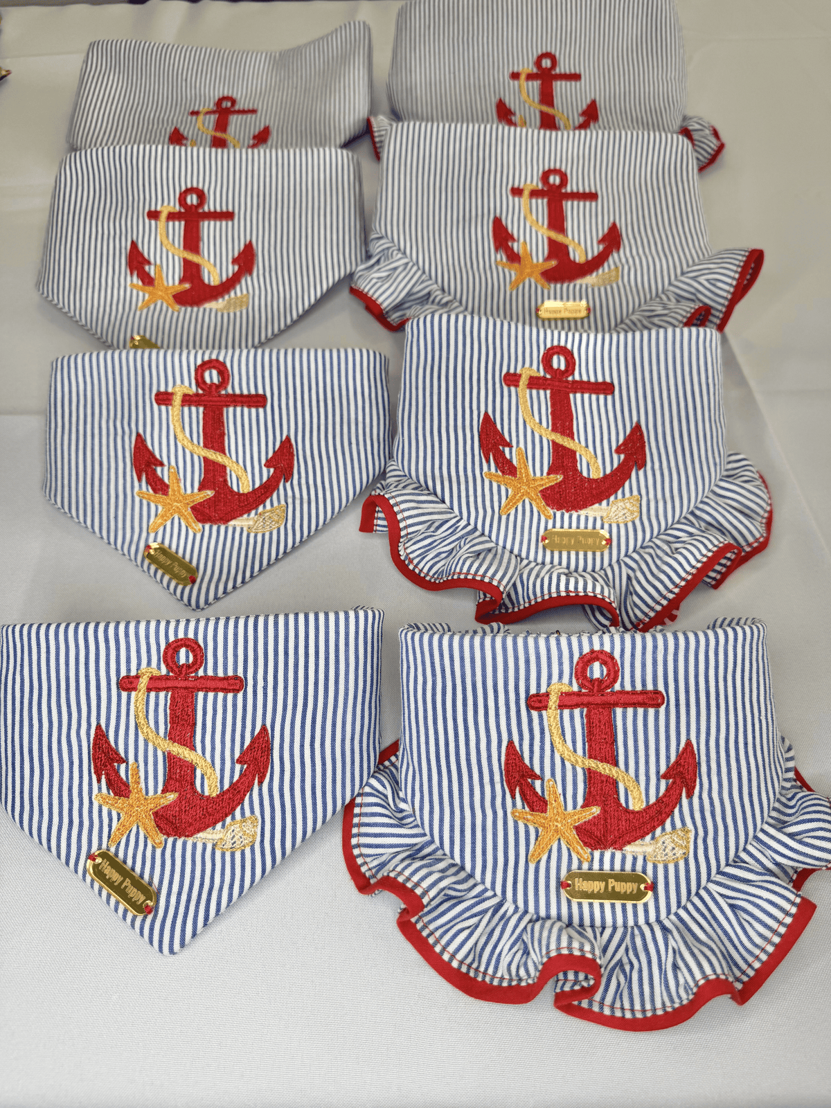 Bandana para perro Beach Anchor de Happy Puppy Bandanas, tela de rayas azul marino y blanco con ancla y estrella de mar bordadas en rojo, vista de grupo con modelos de volante rojo
