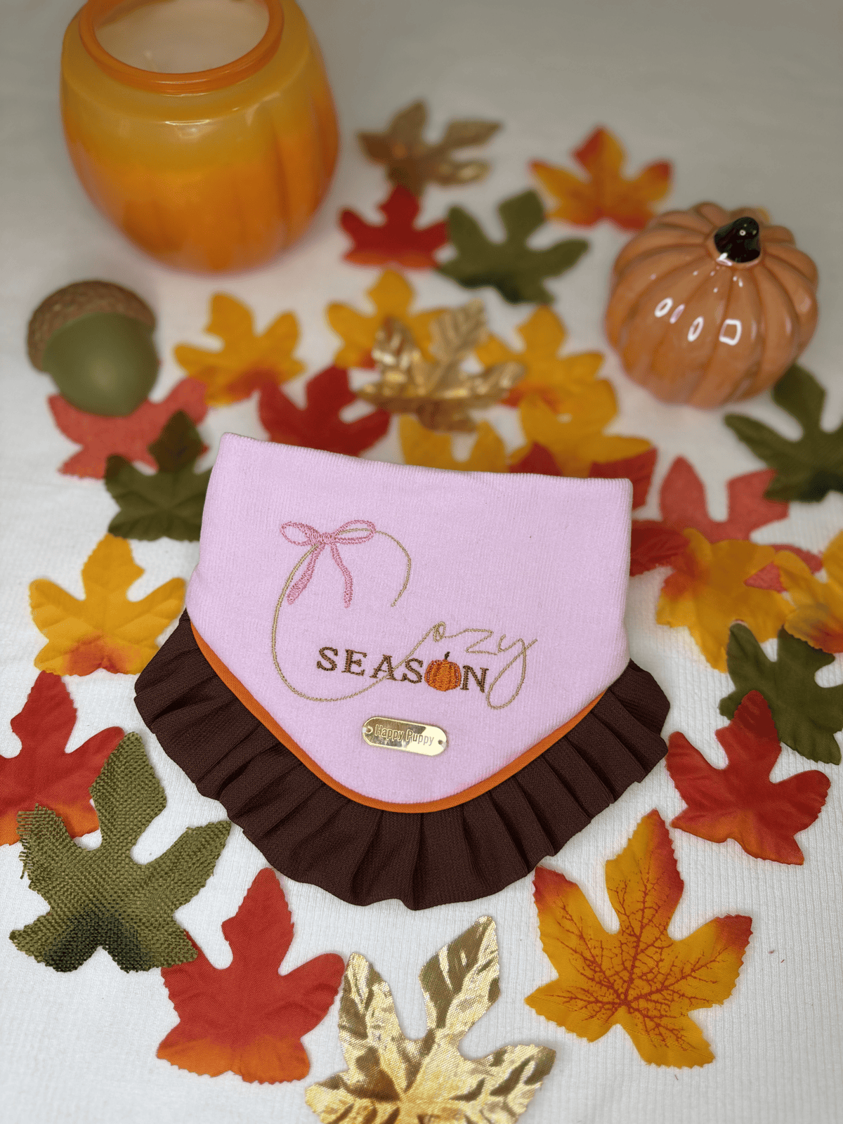 Detalle de la bandana para perro Cozy Season de Happy Puppy Bandanas en rosa con ribete naranja y volante marron, sobre hojas de otono