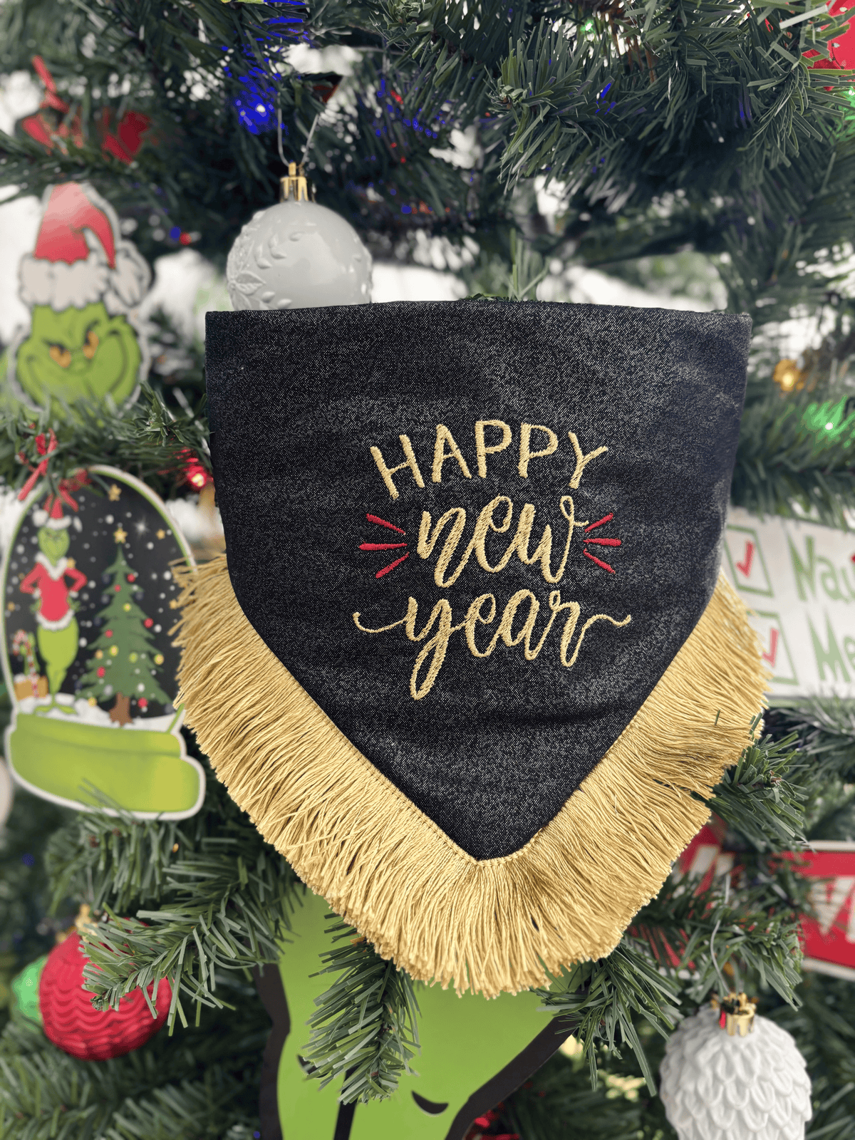 Bandana para perro Happy New Year de Happy Puppy Bandanas, negra con letras Happy New Year bordadas en dorado y fleco dorado, colgada en un arbol de Navidad
