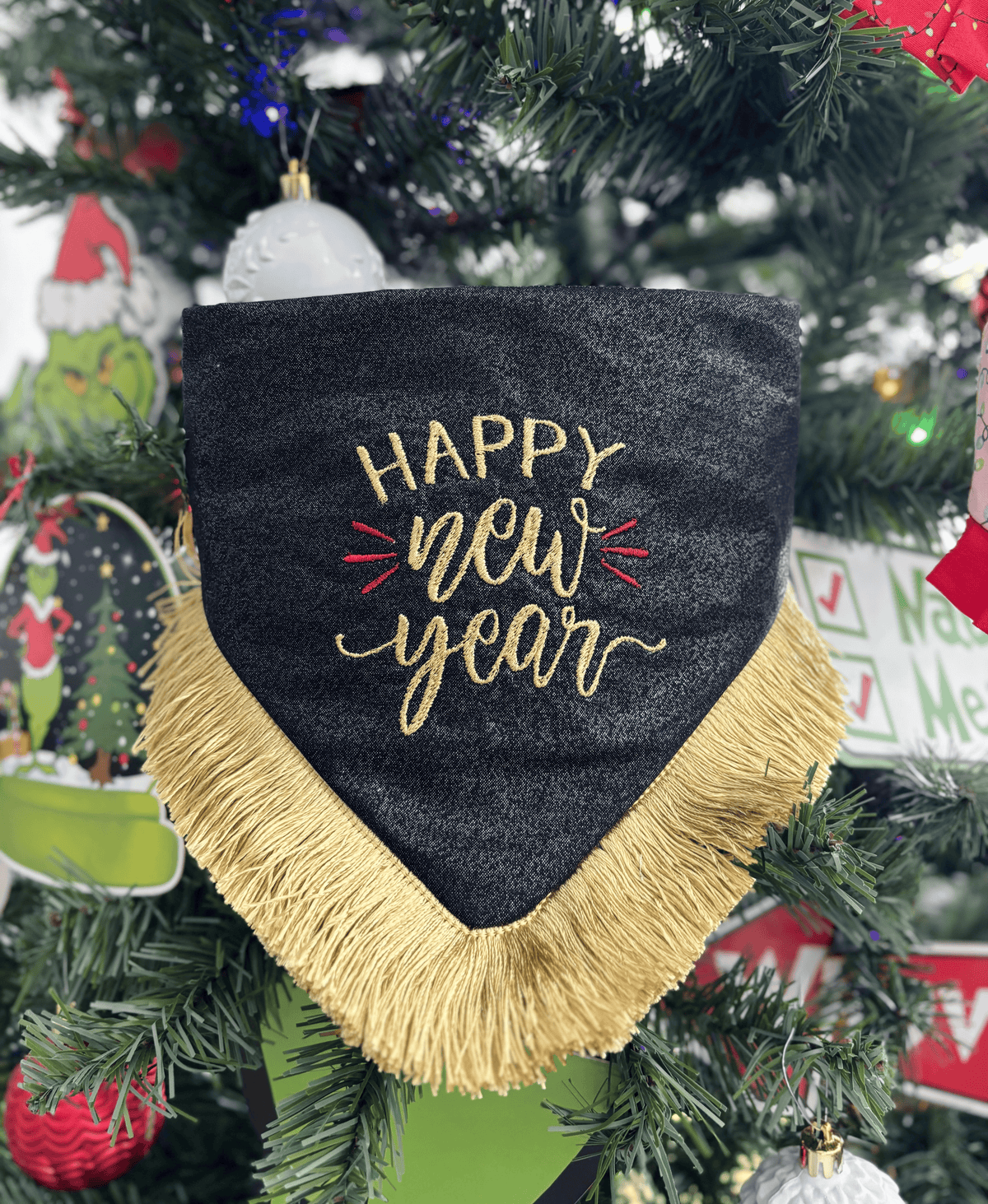 Detalle de la bandana para perro Happy New Year de Happy Puppy Bandanas, negra con letras bordadas en dorado y fleco dorado, sobre un arbol de Navidad