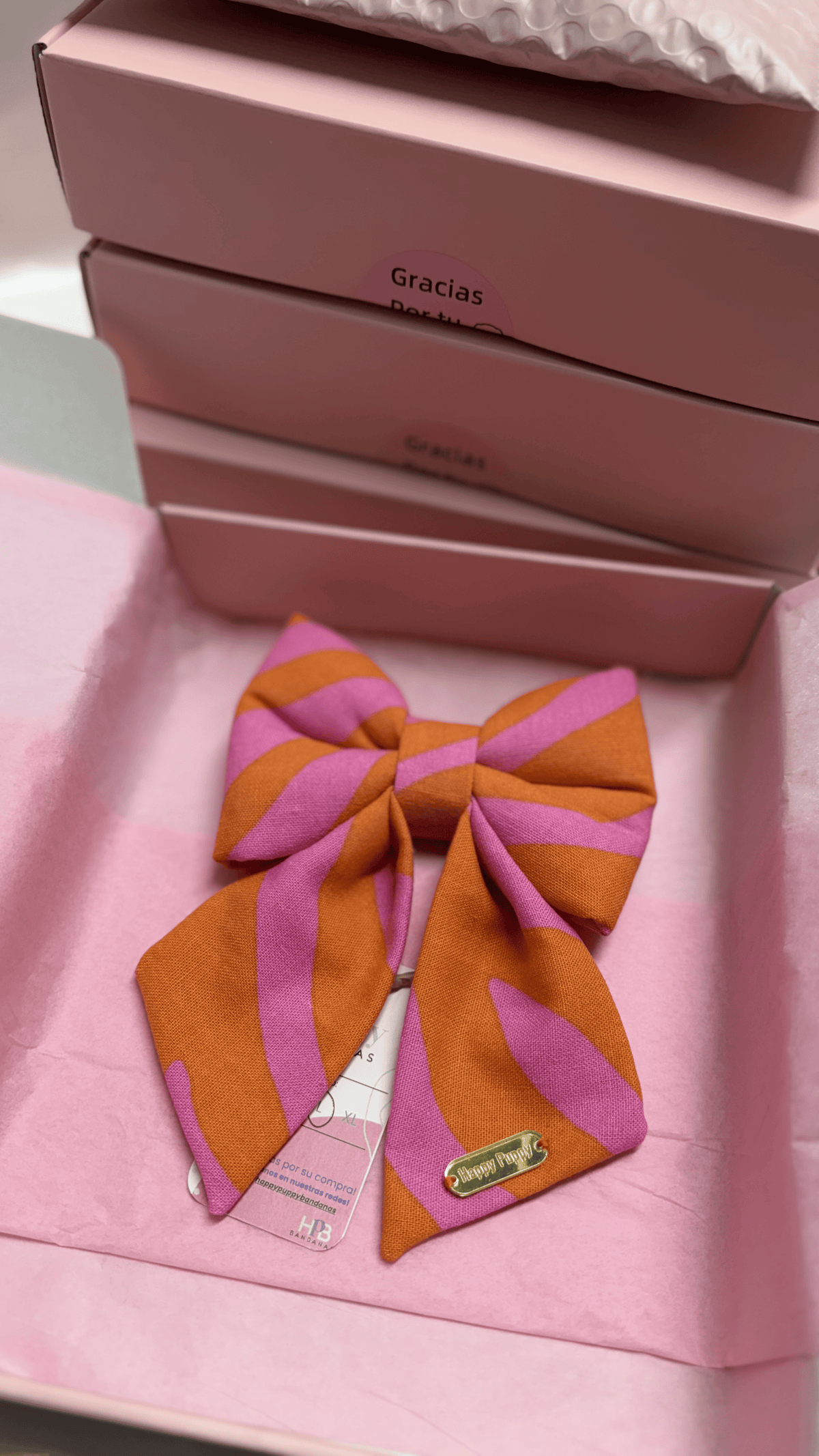 Sailor bow para collar de perro Pink Sailor Bows de Happy Puppy Bandanas en rayas rosa y naranja, vista frontal sobre caja de regalo