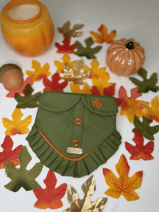 Bandana para perro Pumpkin Patch de Happy Puppy Bandanas en verde oliva con botones naranja y volante naranja, vista frontal sobre hojas y calabazas de otono