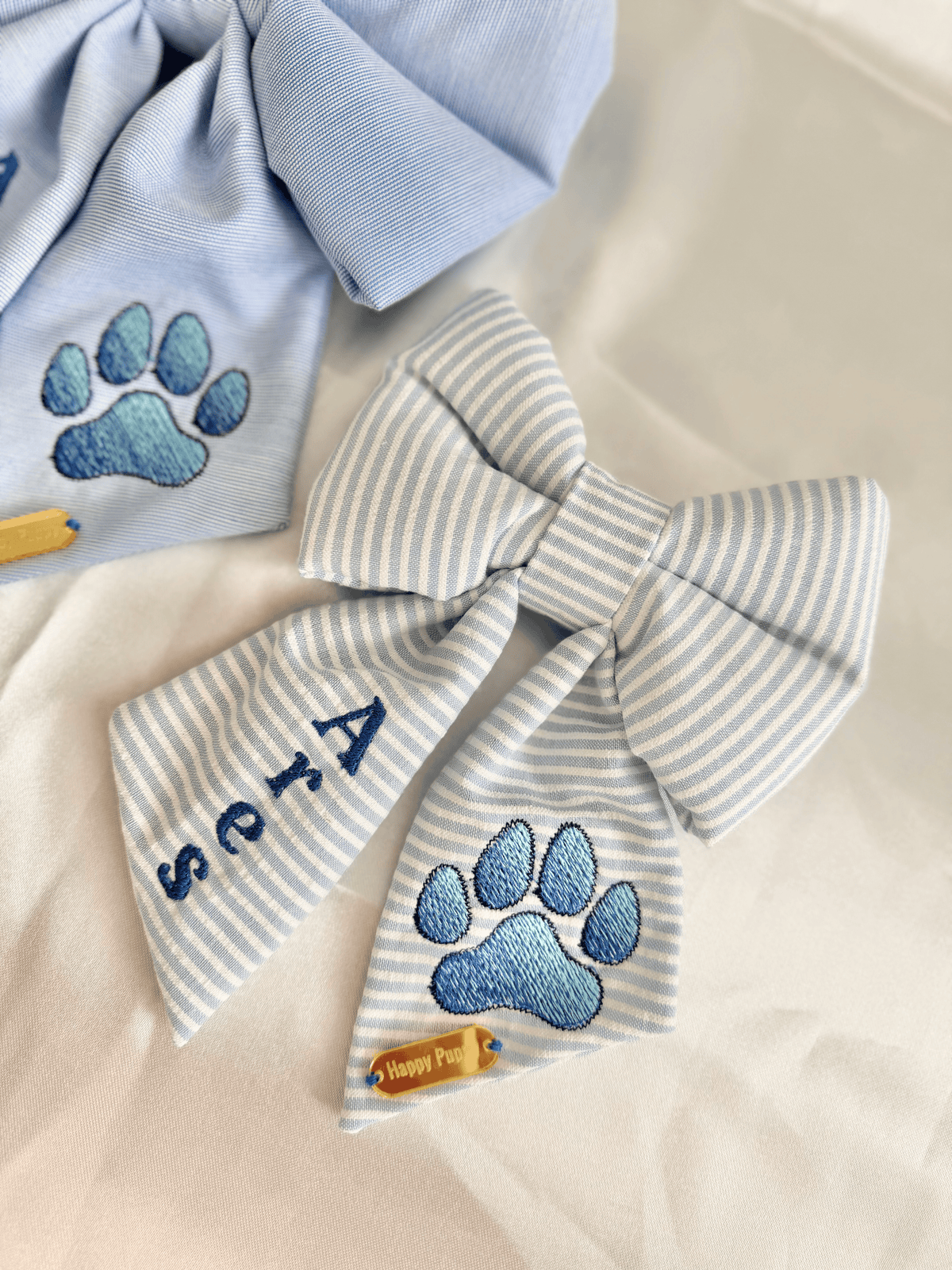 Detalle de sailor bow y bow tie personalizados para collar de perro de Happy Puppy Bandanas, rayas azul claro con huella y nombre bordados en azul