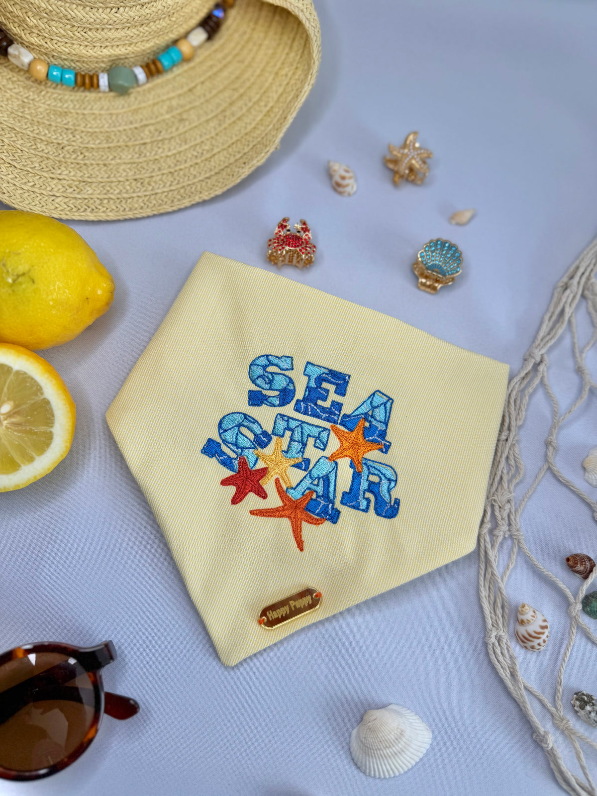 Bandana para perro Sea Star de Happy Puppy Bandanas en amarillo claro con las palabras Sea Star bordadas a color y estrella de mar, vista frontal en ambiente de playa